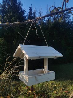 a white bird house hanging from a tree branch in the grass with trees behind it