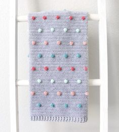 a crocheted blanket hanging on a white ladder with pom - poms