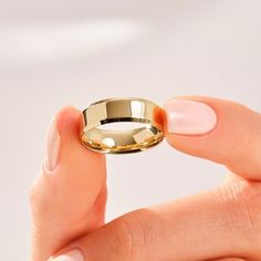 a woman's hand holding a gold wedding ring in front of her face,