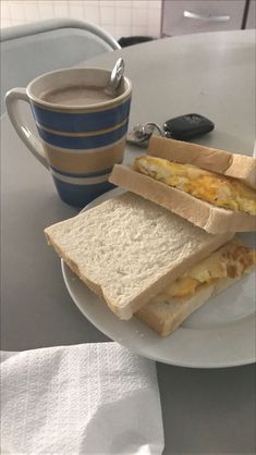 two sandwiches are on a plate next to a cup of coffee and a cell phone