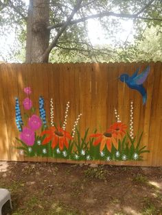 a wooden fence with flowers painted on it and a blue bird flying over the top