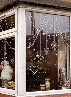 a teddy bear sitting in the window of a store with christmas decorations hanging from it's windows