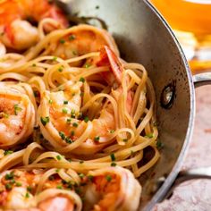 shrimp and pasta with parsley in a skillet next to a glass of beer