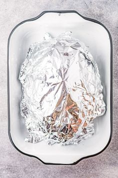 foil wrapped in aluminum foil sitting on top of a white bowl filled with meat and vegetables