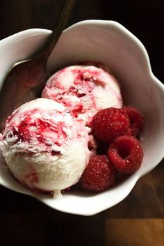 two scoops of ice cream and raspberries in a white bowl