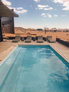 an empty swimming pool in the middle of a sandy area with chaise lounges