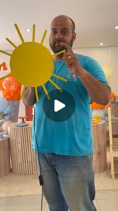 a man holding up a cut out sun in front of his face while standing next to balloons