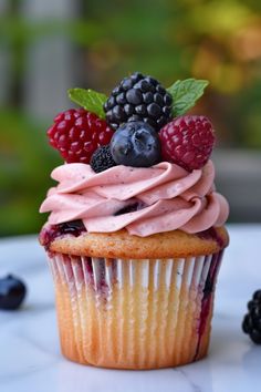 a cupcake with frosting and berries on top sitting next to some blackberries