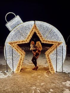 a woman holding a baby in front of a star shaped christmas light display at night