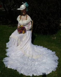 a woman in a white dress and hat sitting on the grass wearing a flower bouquet