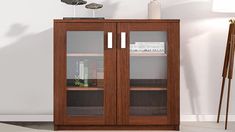 a bookcase with two glass doors in front of a white wall and floor lamp