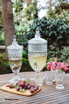 there are three wine glasses sitting on the table with grapes and flowers in front of them