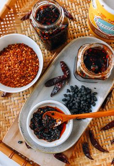 two bowls filled with different kinds of food on top of a wooden tray next to jars and spoons