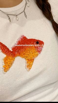 a woman wearing a white shirt with an orange and yellow fish on it's chest