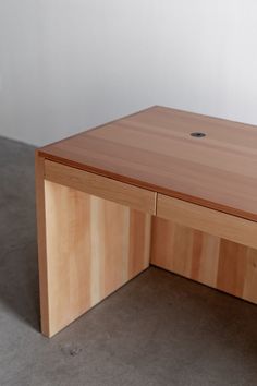 a wooden desk sitting on top of a floor next to a white wall with a hole in it