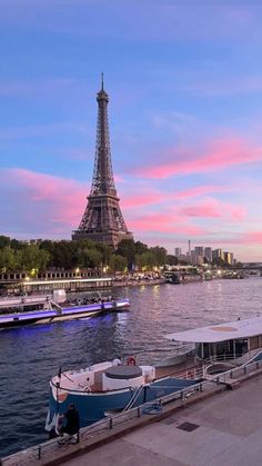 the eiffel tower is lit up in pink and blue as boats are docked on the water