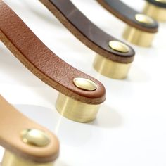 four different colored leather and brass handles on a white surface