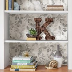 two bookshelves with letters and plants on them in front of a wallpapered background