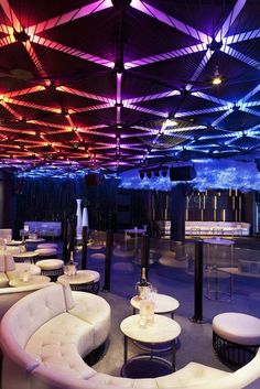 a large room filled with white couches and tables covered in colorful light beams above them