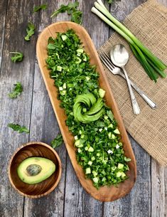 an avocado salad in a wooden bowl next to spoons and utensils