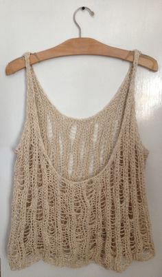 a crocheted top hanging on a wooden hanger next to a white wall