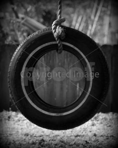 black and white photo of tire hanging from rope