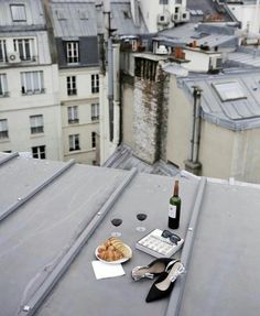 a bottle of wine and some food on top of a roof with buildings in the background