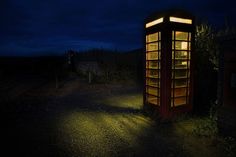 a phone booth sitting in the middle of a field at night with its lights on