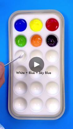 a person holding a paintbrush in front of a white and blue tray with six different colored paints