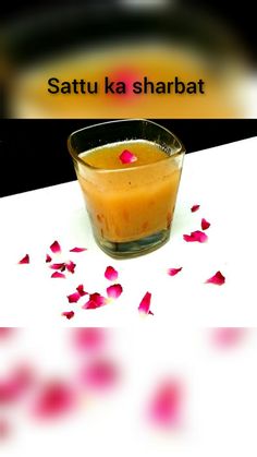 a small glass filled with liquid on top of a white table next to rose petals