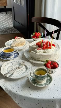 a table topped with cake and plates covered in strawberries on top of a white table cloth