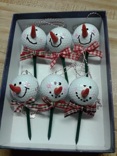 six golf balls decorated like snowmen with red noses and bows tied to them in a box