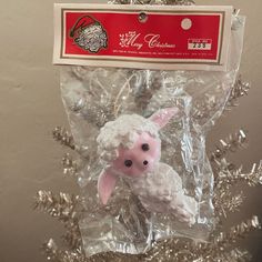 a white sheep ornament hanging from a christmas tree with tinsel on it