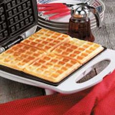 a waffle maker on a table next to some plates and utensils with red napkins