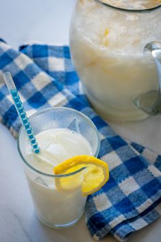 a pitcher of lemonade next to a glass with ice and a blue and white checkered towel