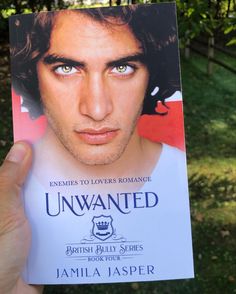 a man holding up a copy of the book unwanted by jamie jasperr, which is in front of some trees