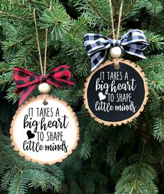 two ornaments hanging from a christmas tree decorated with bows and saying it takes a big heart to shape little minds