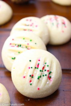 some cookies with sprinkles and white frosting on a wooden table together