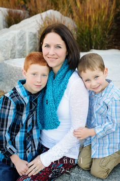 a woman and two boys are sitting on some rocks with their arms around each other