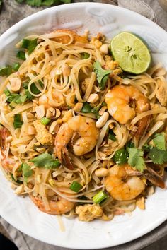 a white bowl filled with noodles and shrimp on top of a table next to lime wedges