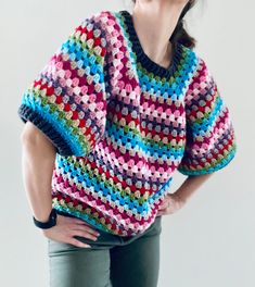 a woman wearing a colorful crocheted sweater with her hands on her hips