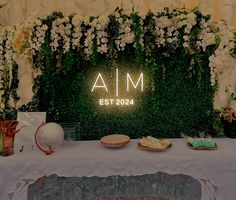 a table topped with plates and cake next to a wall covered in greenery that says aim