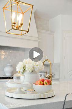 a white kitchen with marble counter tops and gold accents on the light fixture over the sink