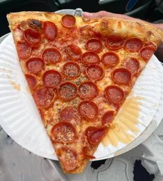 a slice of pepperoni pizza is on a paper plate in someone's hand