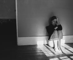 a black and white photo of a woman sitting on the floor with her head in her hands