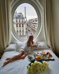 a woman sitting on a bed in front of a round window with the eiffel tower in the background