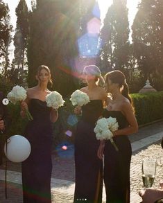 three beautiful women standing next to each other holding white flowers and balloons in their hands