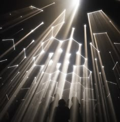 people are standing in front of bright lights on a dark stage with white beams shining from the ceiling