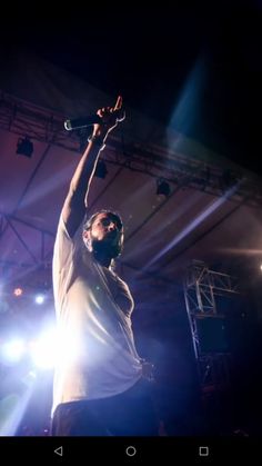 the man is holding his arms up in the air while singing into microphones on stage