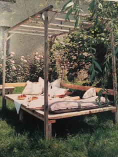 a bed sitting in the middle of a lush green field next to a wooden structure